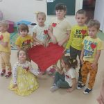 Ośmiro dzieci trzyma w rękach ogromne papierowe czerwone serce.