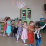 Dzieci w odświętnych ubraniach tworzą pociąg trzymając się za ramiona.