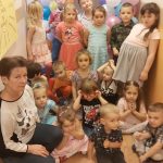 Duża grupa dzieci w balowych ubraniach pozuje do zdjęcia. Część dzieci stoi. Przedszkolaki na pierwszym planie oraz nauczycielka siedzą na podłodze.