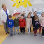 Dzieci w kolorowych strojach stoją wraz z nauczycielką i śpiewają hymn.
