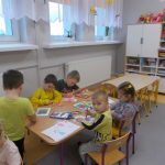 Dzieci w żółtych koszulkach siedzą przy stoliku tworząc prace plastyczne.