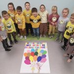 Dzieci stoja ustwone w półkole. Przed nimi na podłodze leży wykonna przez nich praca złożona z kolorowych balonów, splecionych ze sobą.