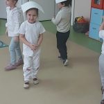 Dzieci poruszają się wolno po sali trzymając białą kartkę na głowie.
