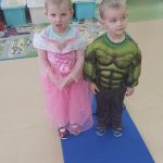 Dziewczynka w różowej sukience i chłopczyk przebrany w strój Shreka stoją na granatowym dywanie