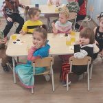 Dzieci w strojach karanwałowych siedzą przy stoliku i odwracają głowy w kierunku obiektywu aparatu.