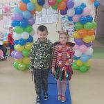 Chłopczyk i dziewczynka w strojach karnawałowych pozują do zdjęcia na tle łuku z kolorowych balonów.