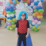 Chłopczyk w stroju karnawałowy niebieskiej peruce pozuje do zdjęcia na tle łuku z kolorowych balonów.