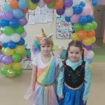 Dwie dziewczynki w strojach karnawałowych pozują do zdjęcia na tle łuku z kolorowych balonów.