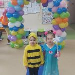 Dwie dziewczynki w strojach karnawałowych pozują do zdjęcia na tle łuku z kolorowych balonów.