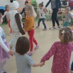 Dzieci tańczą w kółeczku trzymając się za ręce. Bałwanek w środku kółka tńczy z dziewczynką w żółtej bluzeczce i czerwonych spodniach. tańczy w