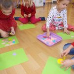 Czwórka dzieci zajmuje się układaniem kolorowych elementów na zielonych podkładkach.