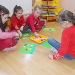 Grupa dzieci siedząca po turecku na podłodze układa obrazki z kolorowych elementów.