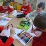 Dzieci przy stoliku, kolorujące obrazek. na stoliku leżą przybory do rysowania: kolorowe kredki, pisaki, piórniki
