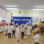 Duża grupa dzieci ubranych w białe stroje bawi się w rytm muzyki