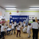 Grupa dzieci ubranych w białe stroe tańczy w rytm mzuyki.