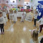 Dzieci ustawione w półokręgu bawią sę białymi wstążkami.