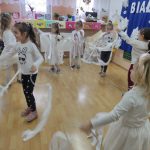 Dzieci ustawione w okręgu tańczą z białymi wstążkami.