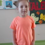 Dziewczynka w pomarańczowej koszulce wykonuje piosenkę