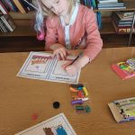 Dziewczynka w blond włosach i różowej bluzeczce rysuje kolorowymi kredkami na kartce